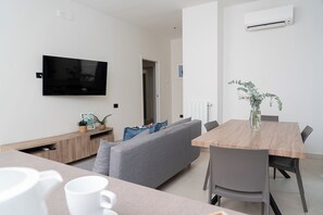 A modern living room with a flat-screen TV, grey sofa, wooden dining table, and a small potted plant. - Via Niccolò Tommaseo 4 - Appartamento 3 (Naples)