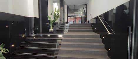 A modern hotel lobby with a staircase, a reception desk, and a sign reading 'TEMA PALACE'.