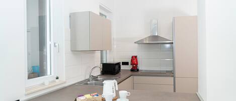 A compact kitchen with a window, a microwave, a red coffee maker, and a small coffee table with cups and a box of tea.