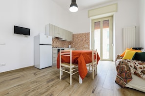 Un espacio habitable compacto con kitchenette, una mesa de comedor con mantel, una cama con ropa de cama colorida y un televisor montado en la pared.