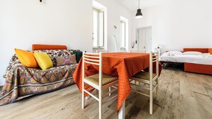 A room with a dining table, a sofa with colorful cushions, a bed with orange bedding, and a wooden floor. - Via Morghen 63 - Primo Piano (Naples)