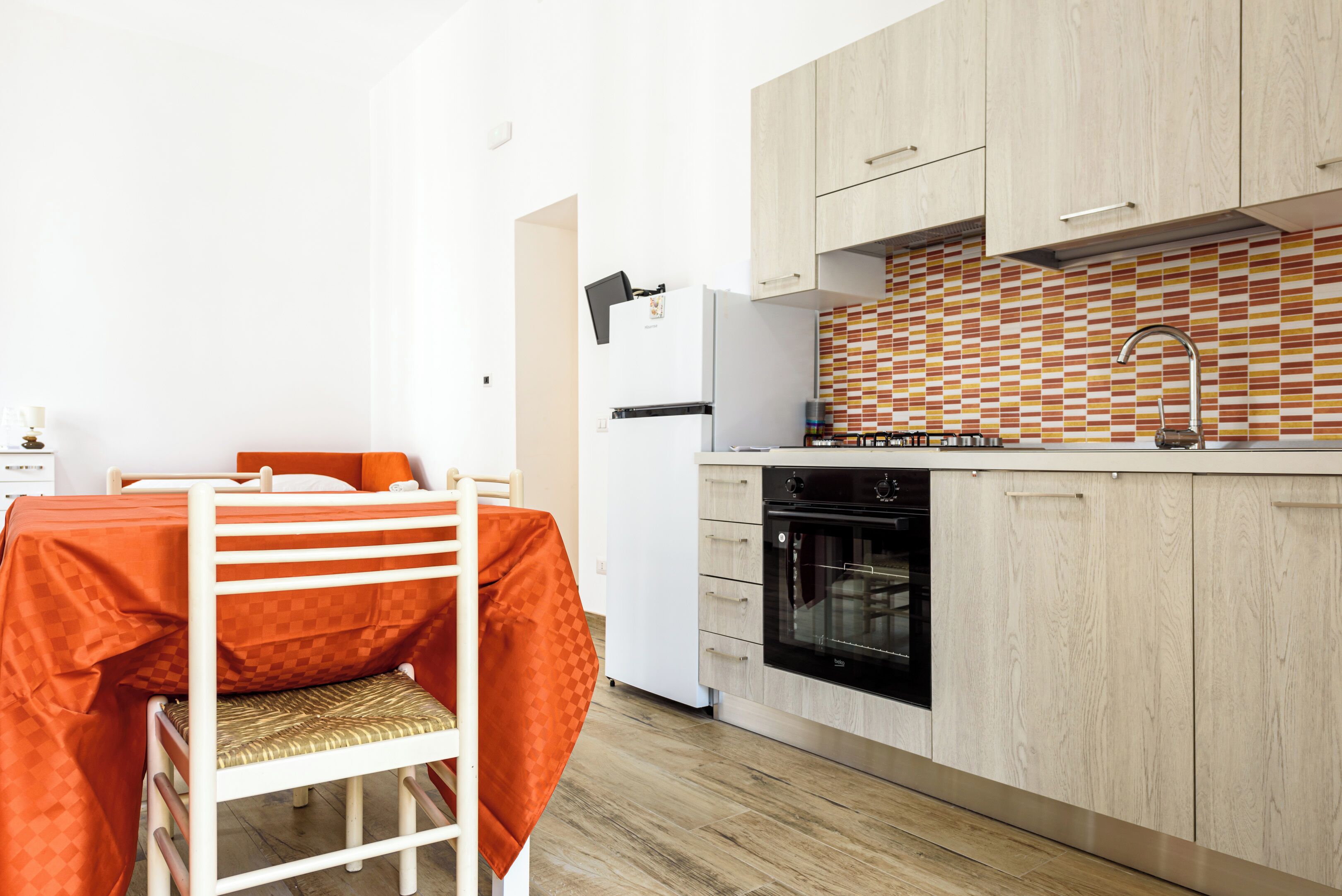 Una cocina compacta con armarios de madera, un refrigerador blanco, un horno negro y un salpicadero de azulejos.