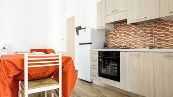 Una cocina compacta con armarios de madera, un refrigerador blanco, un horno negro y un salpicadero de azulejos.