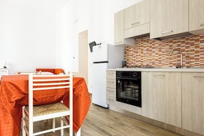 A compact kitchen with wooden cabinets, a white refrigerator, a black oven, and a tiled backsplash. - Via Morghen 63 - Primo Piano (Naples)