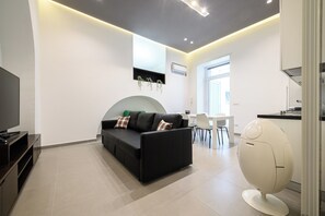 A modern living room with a black sofa, a flat-screen TV, and a unique egg-shaped chair. - Via Morghen 63 (Naples)