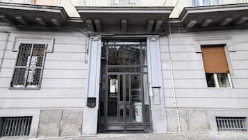 L'ingresso di un edificio con una porta in vetro, una piccola finestra con persiana e un balcone con ringhiere.