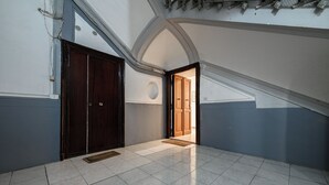 Een gang met een betegelde vloer, een houten deur en zicht op een andere kamer.