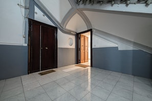 A hallway with a tiled floor, a wooden door, and a view into another room. - Via Morghen 63 (Naples)