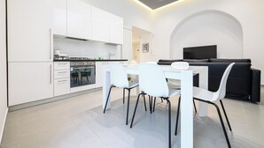 Een moderne keuken met witte kasten, een eettafel met stoelen en een zwarte bank in een woonruimte met een televisie.