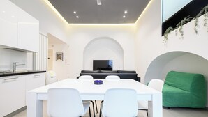 Een moderne keuken met witte kasten en een zwart aanrecht, een eethoek met een witte tafel en stoelen, een zwarte bank en een groene fauteuil.