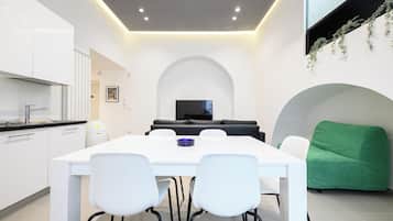 Una cucina moderna con mobili bianchi e un piano di lavoro nero, una zona pranzo con tavolo e sedie bianche, un divano nero e una poltrona verde.