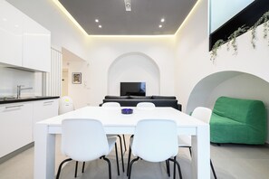 A modern kitchen with white cabinets and a black countertop, a dining area with a white table and chairs, a black sofa, and a green armchair. - Via Morghen 63 (Naples)