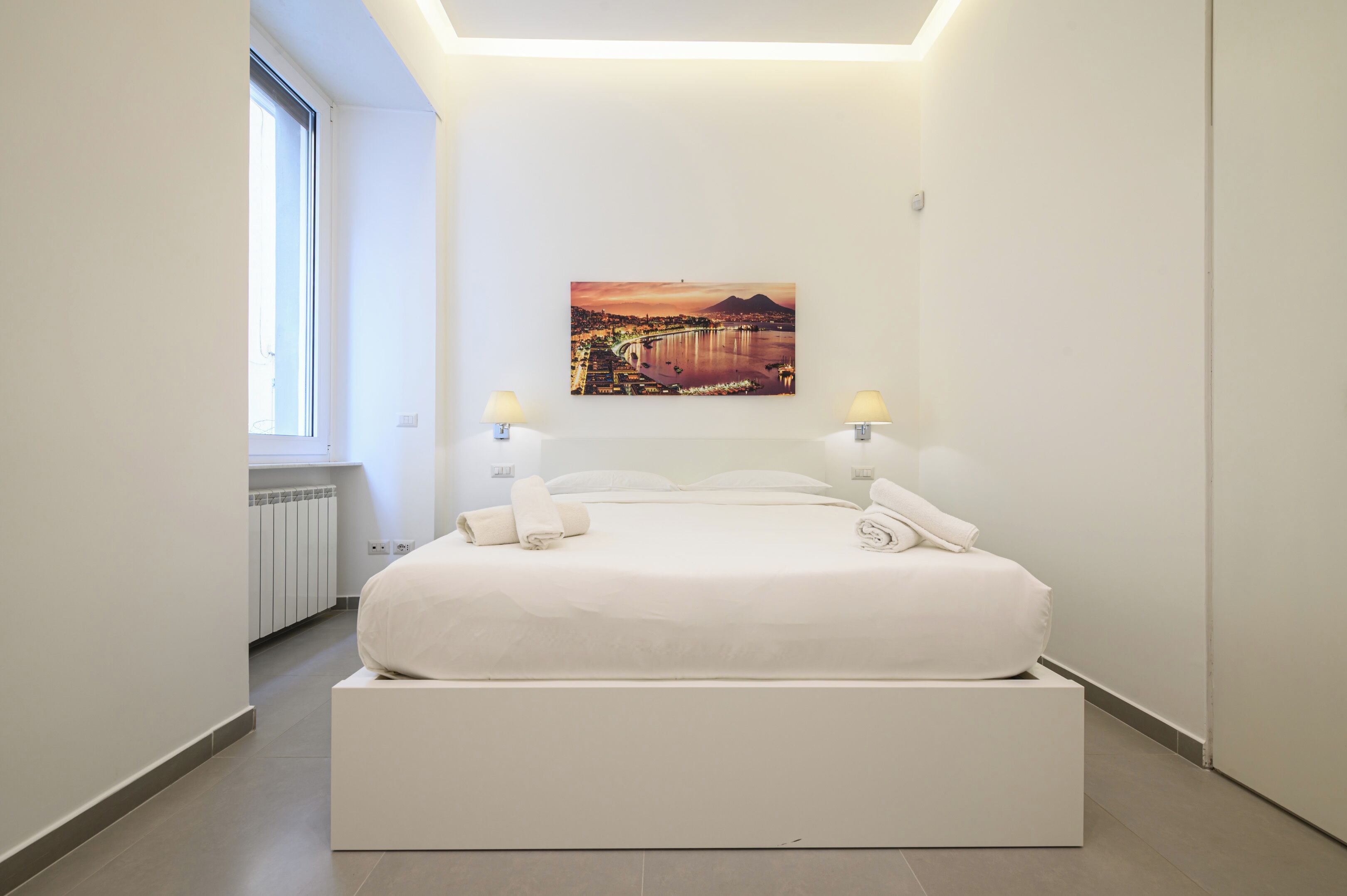 A modern bedroom with a large bed, a cityscape painting on the wall, and two bedside lamps.