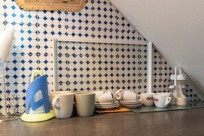 A kitchen with blue and white patterned tiles, a white shelf, and various kitchen items including mugs, plates, and a coffee maker. - Il Nido (Naples)