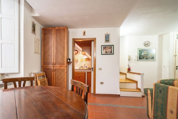 A dining area with a wooden table and chairs, a kitchen visible through a wooden door, and a staircase leading to another level. - Il Nido (Naples)
