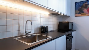 Een moderne keuken met een roestvrijstalen spoelbak, zwarte apparaten, witte kasten en een betegelde spatwand.