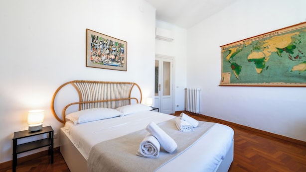 Een net opgemaakt bed met een houten hoofdbord, een klein nachtkastje met een lamp, en een wereldkaart aan de muur.
