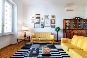 Ein Wohnzimmer mit einem Schachbrettteppich, zwei gelben Sofas, einem Holzschrank und gerahmten Bildern an der Wand.