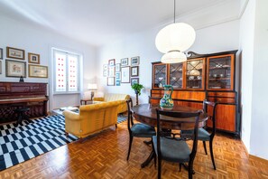 Un coin repas comprenant une table en bois, des chaises, un piano, un canapé et un buffet aux portes vitrées.