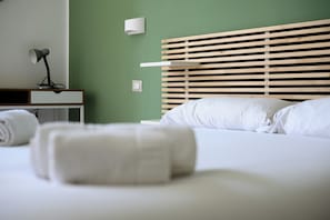 A neatly made bed with white linens, a wooden slat headboard, a bedside lamp, and a wall-mounted light fixture. - Via Cairoli 60 (Naples)