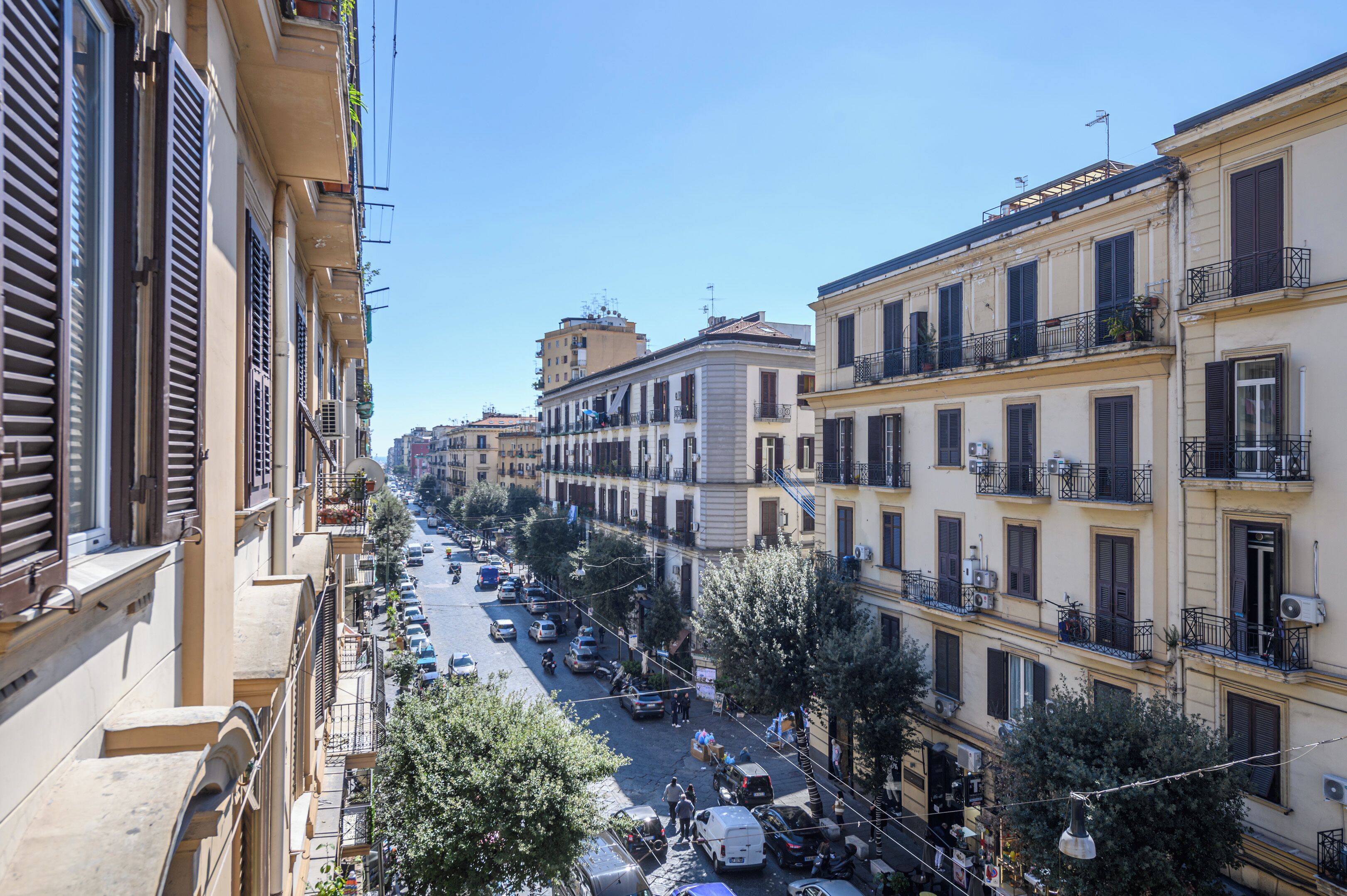 A street view with multi-story buildings, parked cars, and trees.