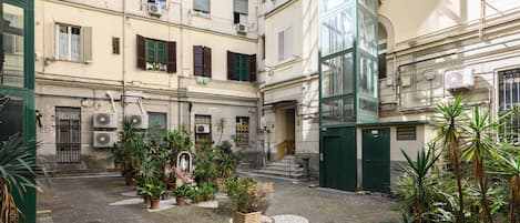 A courtyard with potted plants, a statue, and a staircase leading to a green door.