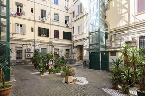 A courtyard with potted plants, a statue, and a staircase leading to a green door. - Via Cairoli 60 (Naples)