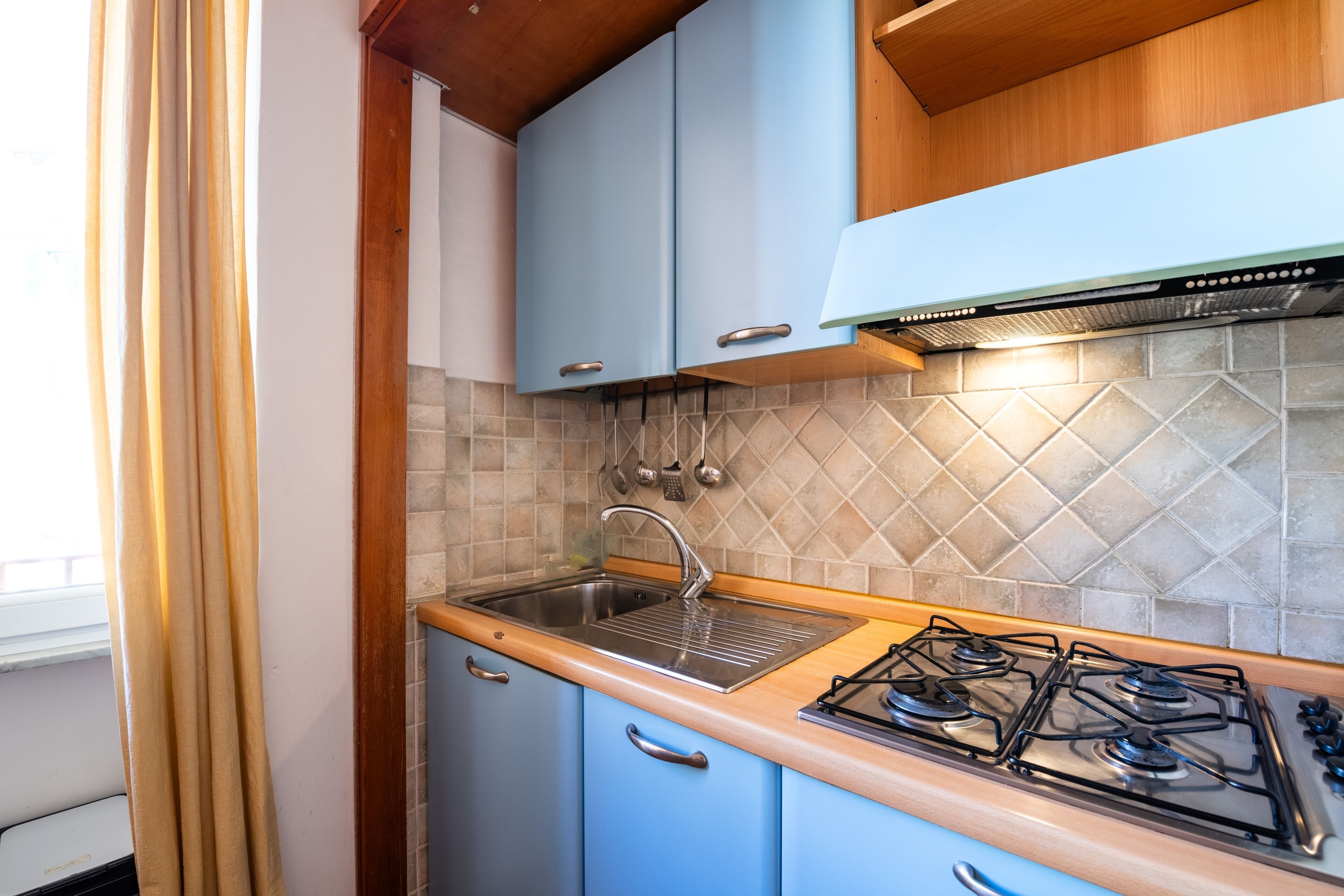 Une cuisine de taille réduite avec des meubles bleus, un évier en acier inoxydable et une cuisinière à gaz.