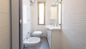 Un bagno stretto con toilette, bidet e lavabo.