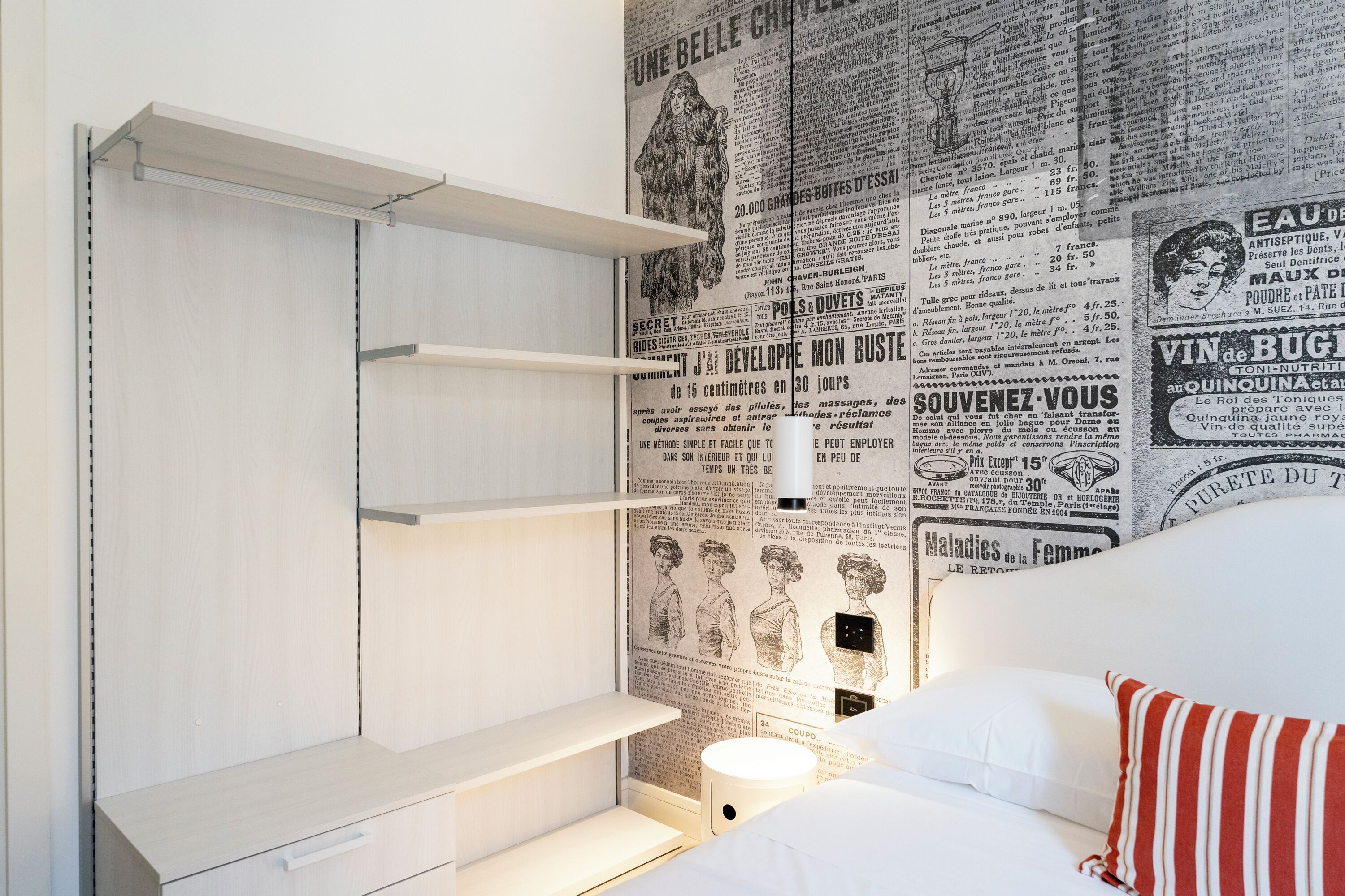 Quarto com cama, mesa de cabeceira e parede com recortes de jornal.