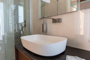Ein modernes Badezimmer mit einem großen, weißen Aufsatzbecken, einer Glasdusche und einer Marmorarbeitsplatte.