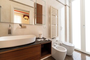 Un bagno moderno con un lavandino bianco di grandi dimensioni, uno specchio, un water e una cabina doccia in vetro.