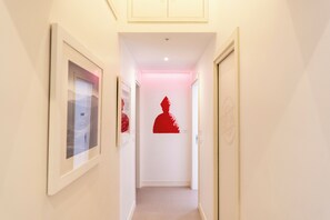 A hallway with framed pictures on the walls, a red silhouette decoration on the wall, and a door on the right. - Via Concezione a Montecalvario 19 (Naples)