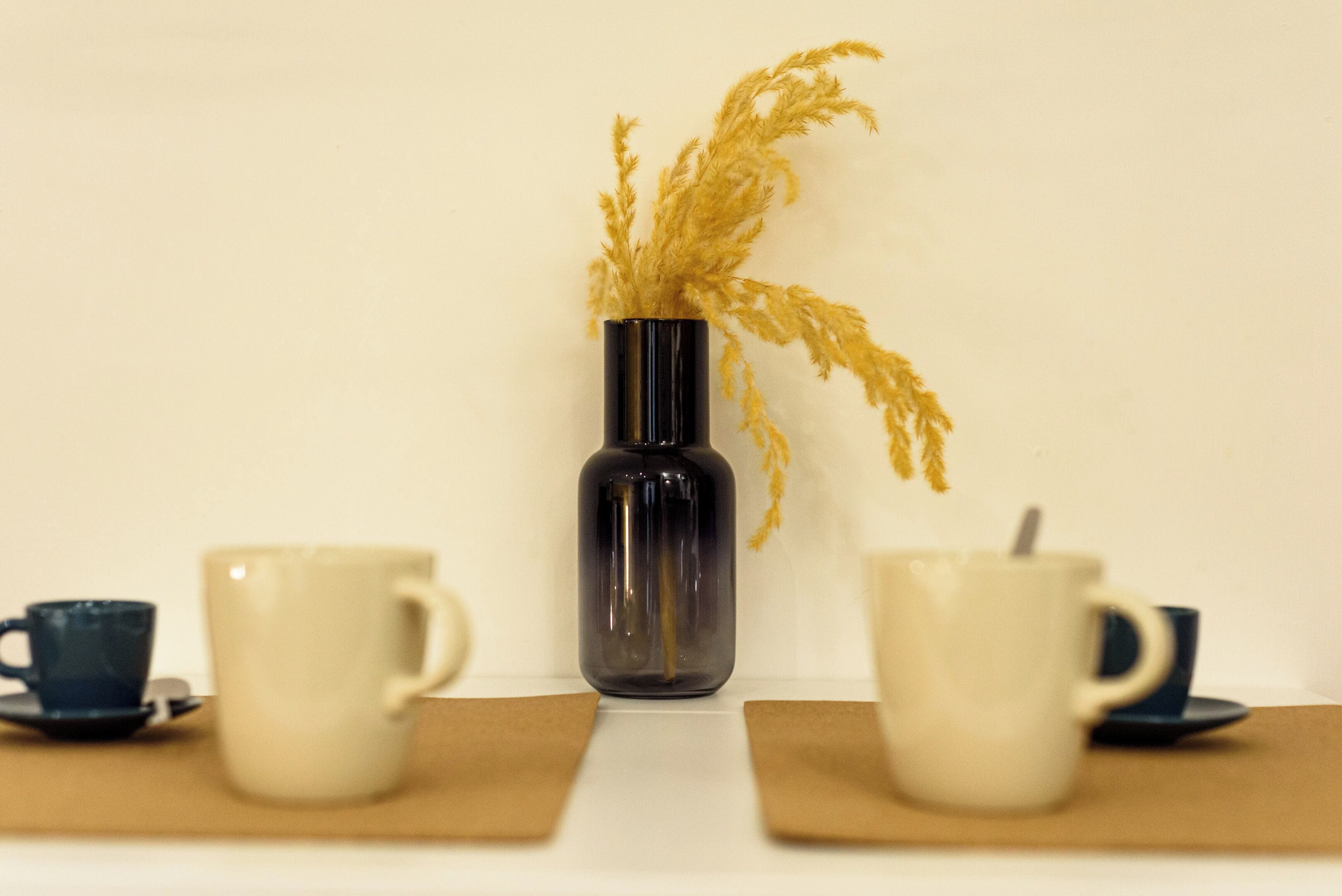 A table with a vase of dried plants, two cups, and a saucer.
