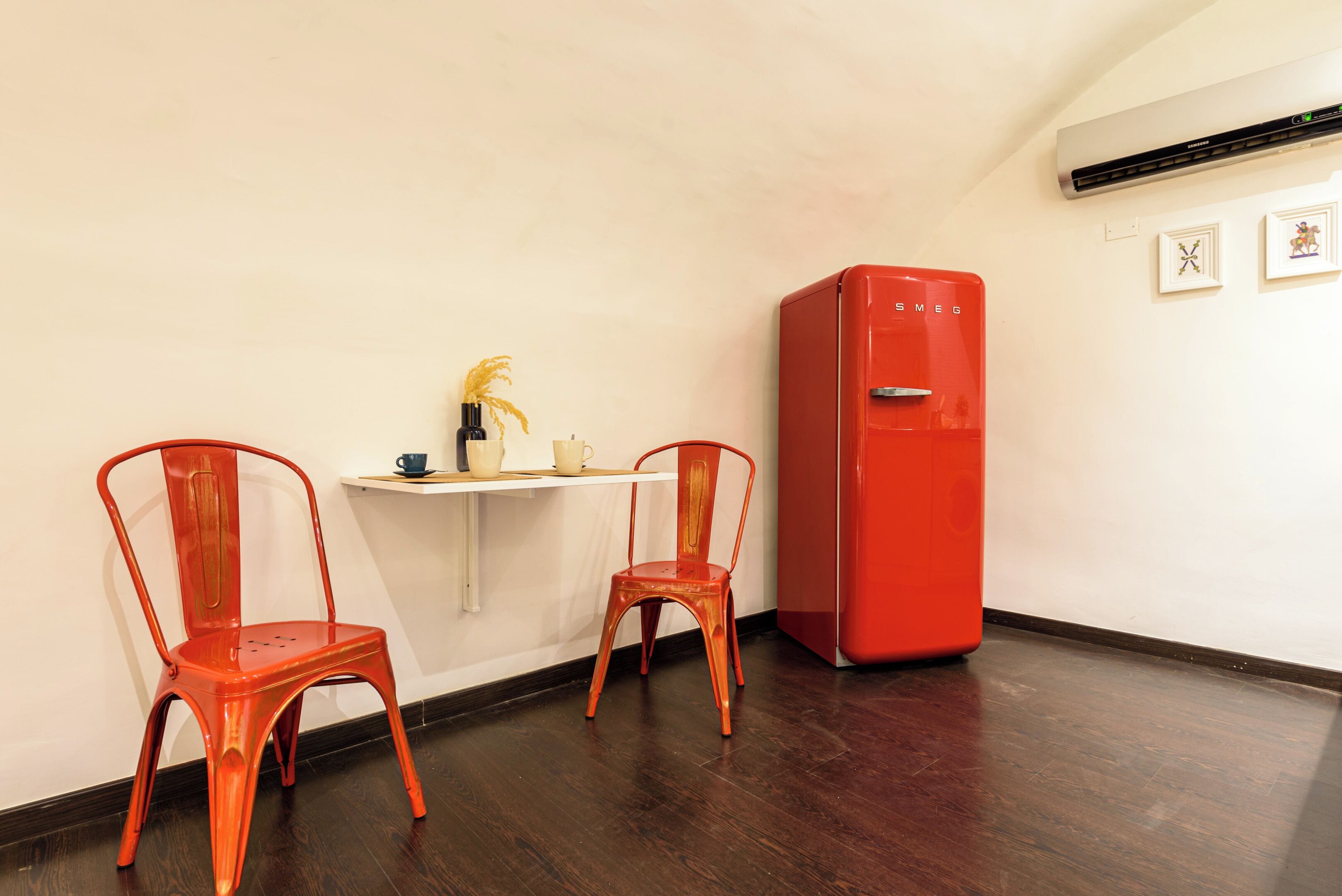 A room with two red chairs, a small white table, and a red refrigerator.