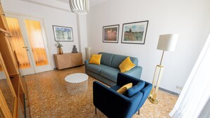 A living room with a blue sofa, a round coffee table, and a floor lamp. There are framed pictures on the wall and a statue on a side table. - Casa Tripolitania (Rome)