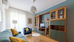 A living room with a blue sofa, a round coffee table, and a wooden cabinet with glass doors. - Casa Tripolitania (Rome)