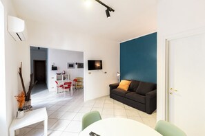 A modern living room with a white dining table, green chairs, a dark sofa with a brown cushion, and a TV mounted on the wall. - Vico Piazza Nuova 1 (Naples)