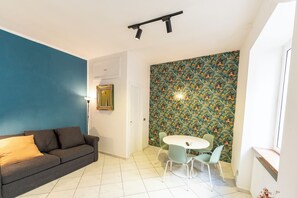 Ein Wohnzimmer mit blauer Wand, einem grauen Sofa, einem weißen Tisch mit zwei Stühlen und einem Wandpapier mit Muster.