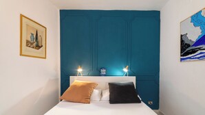 Quarto com cama branca, duas almofadas, parede em tom de verde-água, quadro e ilustração de um mapa.