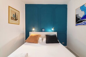 A bedroom with a white bed, two pillows, a teal accent wall, a framed picture, and a map artwork. - Vico Piazza Nuova 1 (Naples)