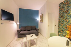 A living room with a blue accent wall, a grey sofa, a white coffee table, and a flat-screen TV mounted on the wall. - Vico Piazza Nuova 1 (Naples)