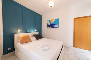 A hotel room with a bed, a blue accent wall, a painting, and a wooden door. - Vico Piazza Nuova 1 (Naples)