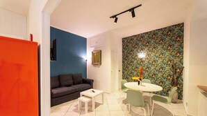 Um espaço de estar compacto com uma parede azul de destaque, uma área de jantar com mesa e cadeiras redondas, e um sofá cinzento.