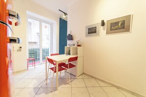 A compact living space with a dining area featuring a white table and red chairs, a small kitchen area, and a balcony with a view. - Vico Piazza Nuova 1 (Naples)