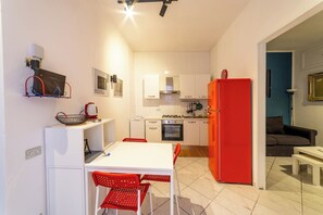 A compact kitchen with white cabinets, a red refrigerator, and a dining area with red chairs. - Vico Piazza Nuova 1 (Naples)