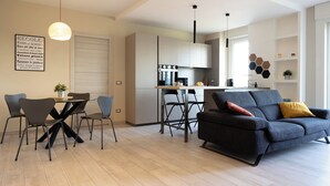 Una sala de estar moderna con sofá, mesa de comedor y sillas. Hay una zona de cocina con estufa y armarios.