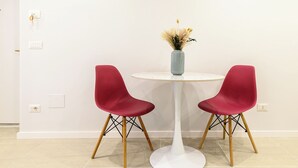 Une table ronde blanche, accompagnée de deux chaises rouges et d’un vase contenant des fleurs séchées.