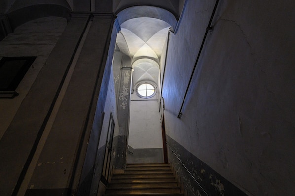 Una estrecha escalera con un ventanal circular en la parte superior, que conduce a un piso superior.