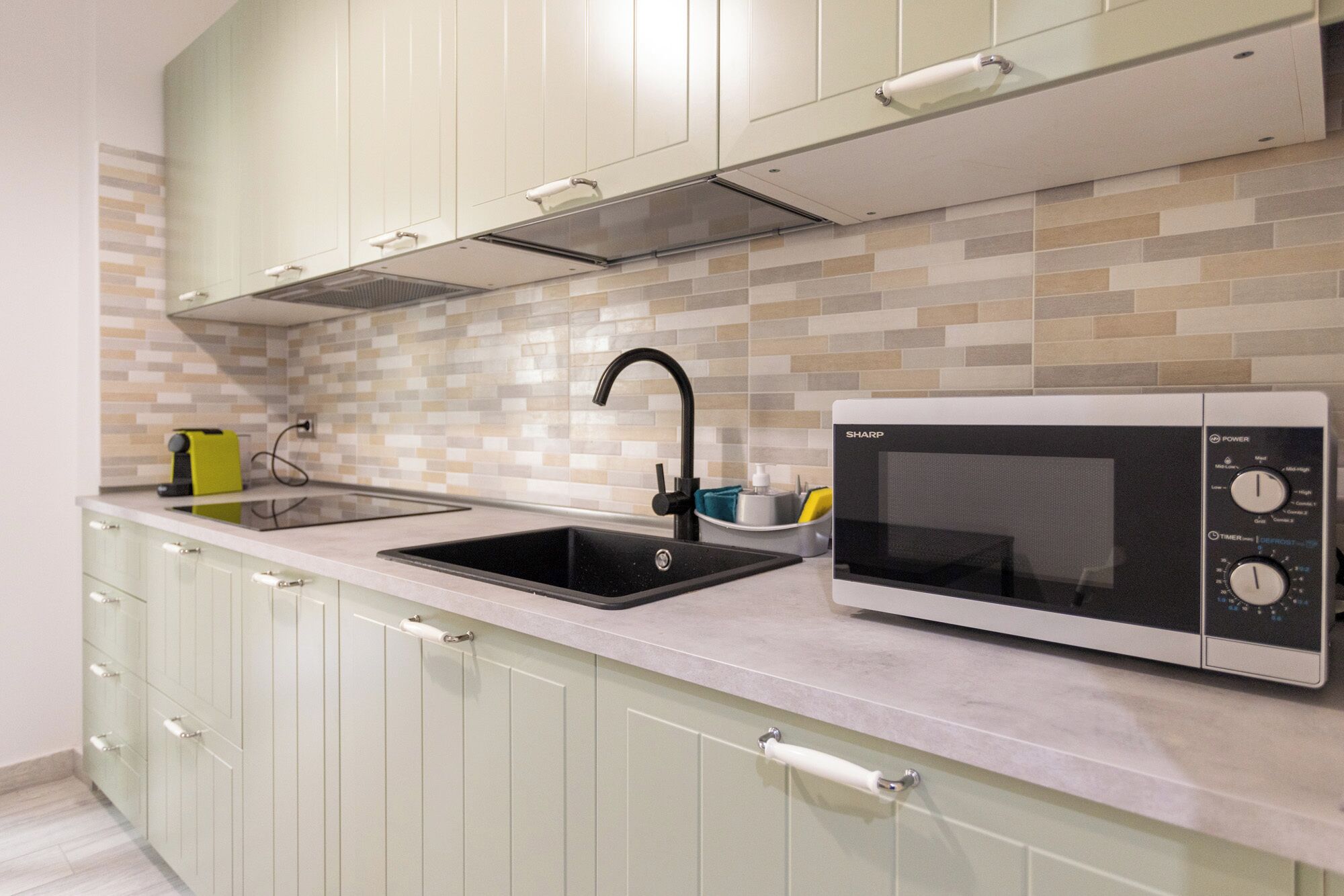 Una cocina moderna con un lavamanos doble, un microondas integrado y armarios de colores claros.